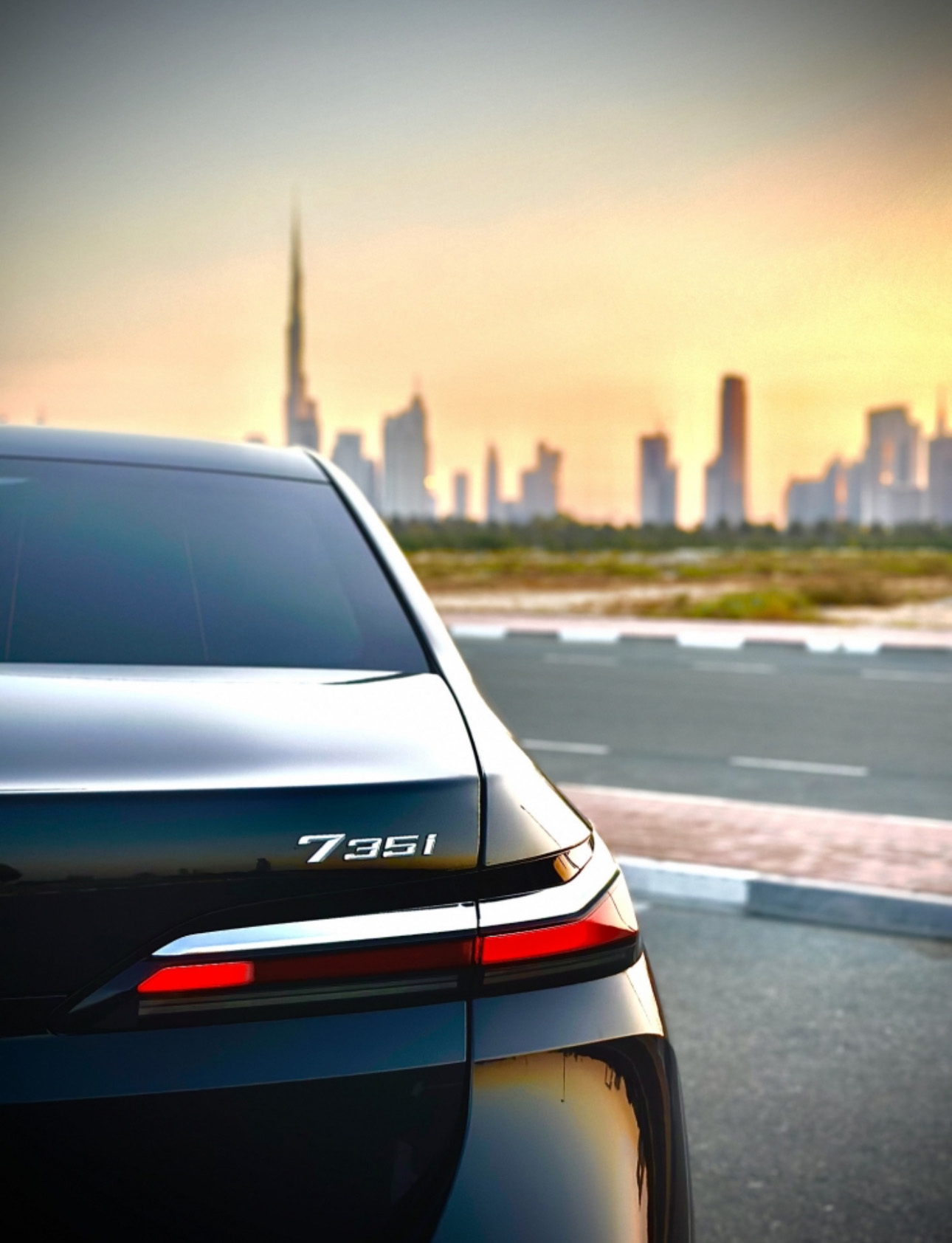 BMW 735i rear view with city skyline at golden sunset