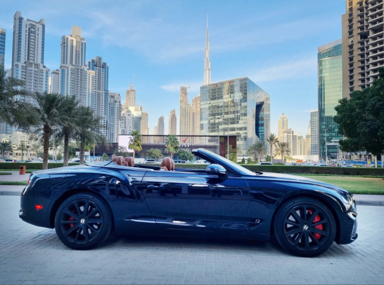 Dark blue convertible Bentley parked in Dubai with skyscrapers backdrop