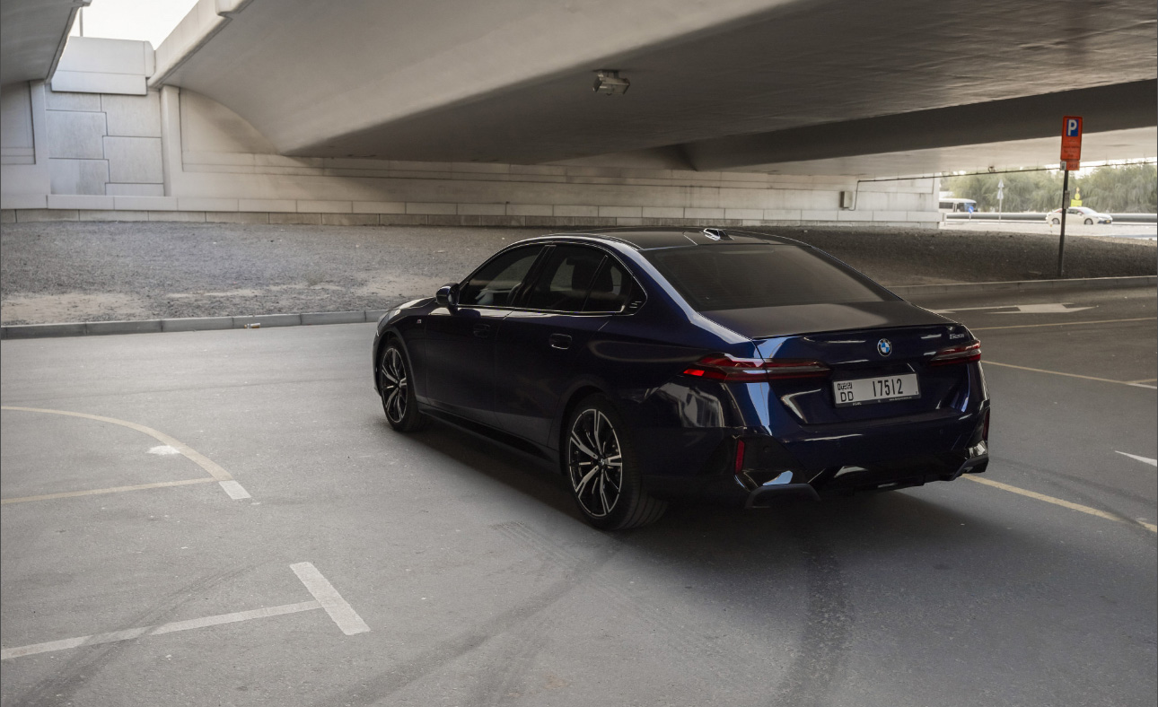 Dark blue BMW sedan parked under concrete bridge in parking area