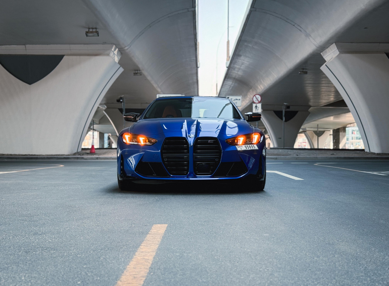 Blue BMW sports car parked in modern concrete tunnel with glowing headlights