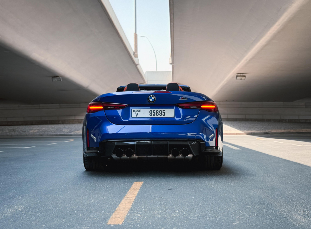 Blue BMW sports car parked under concrete overpass, rear view
