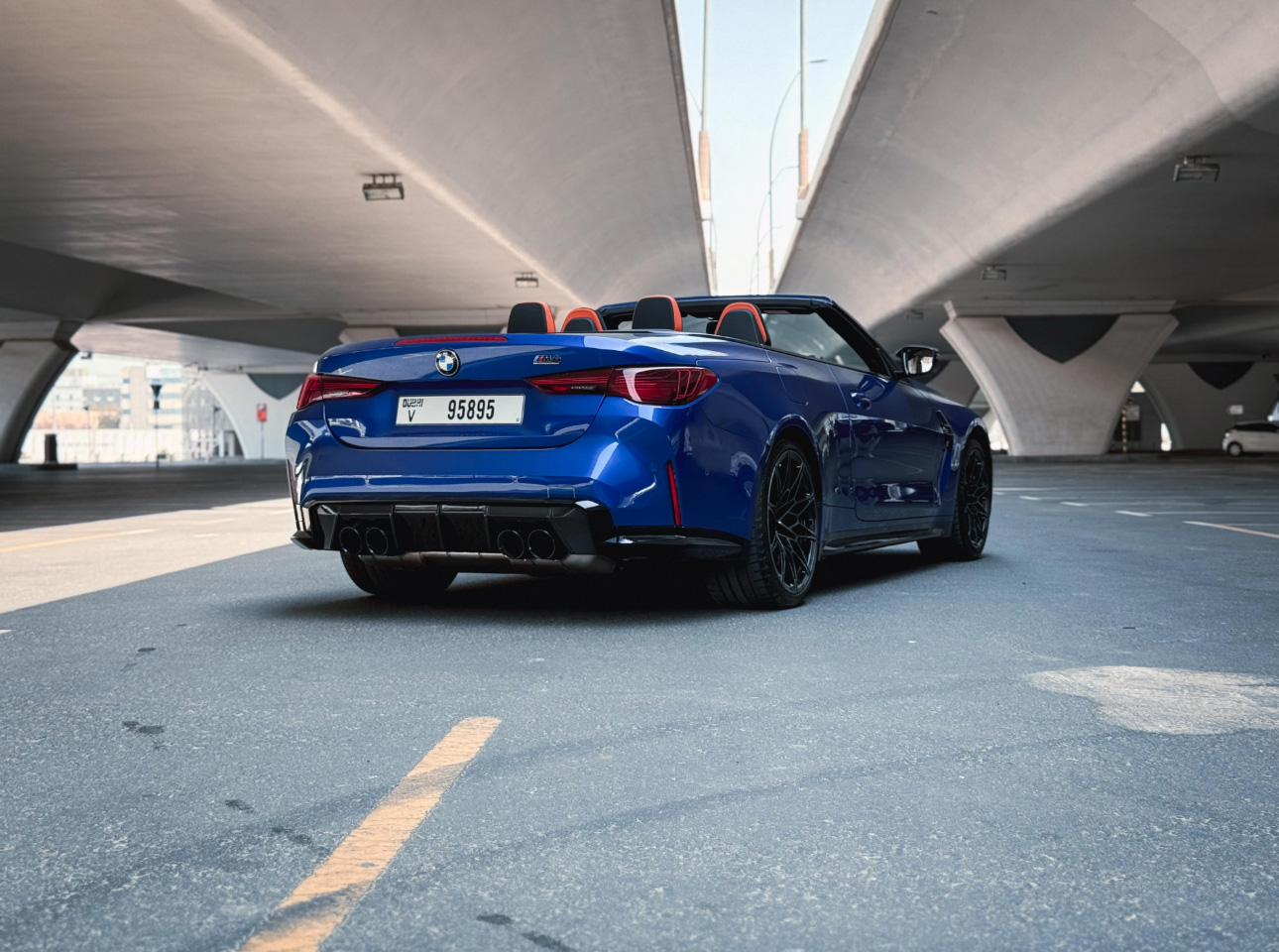 Blue BMW M4 convertible parked under concrete bridge with red interior
