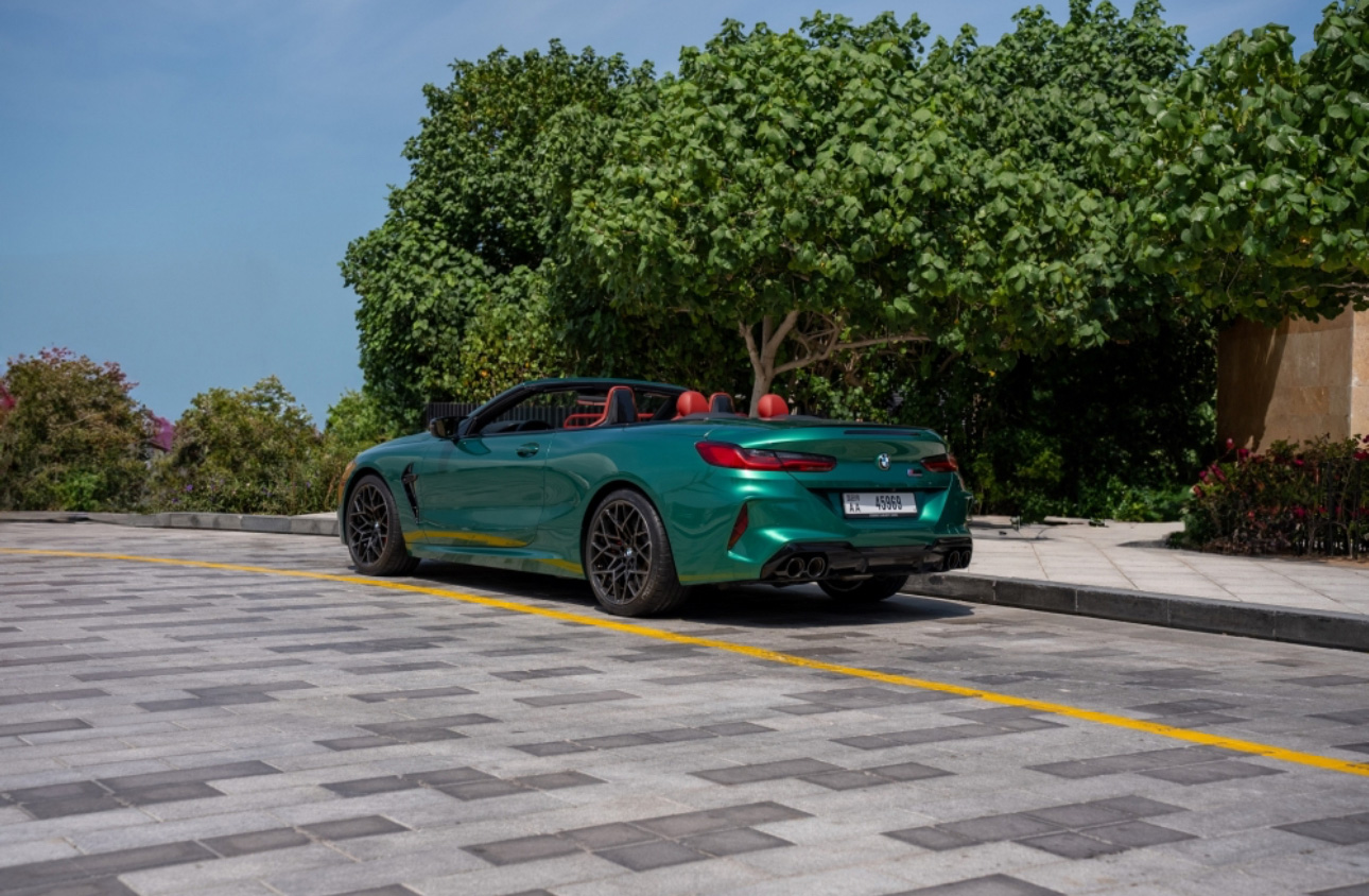 Green BMW convertible parked on tiled ground with trees in background
