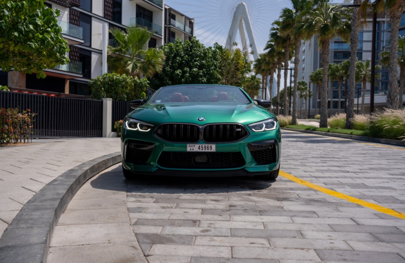 Green BMW sports car parked on a curved street with palm trees