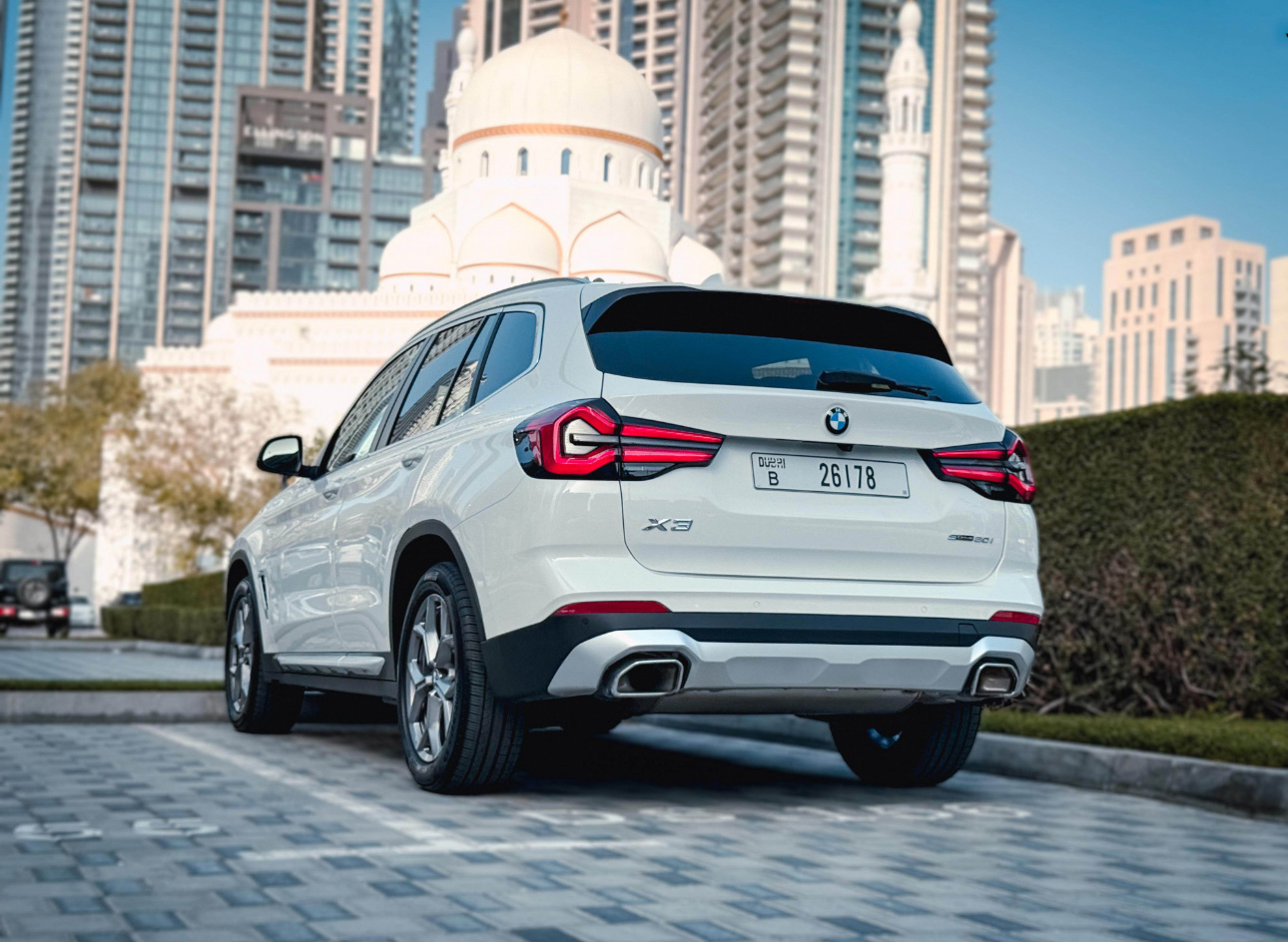 White BMW X3 parked in urban Dubai setting with mosque and skyscrapers