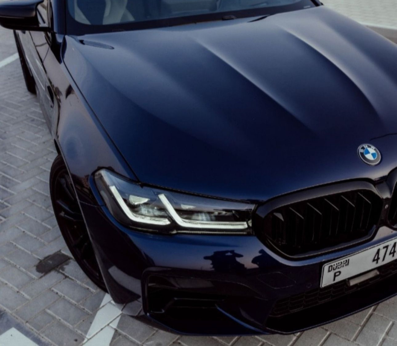 Dark blue BMW with sharp headlights parked on brick pavement