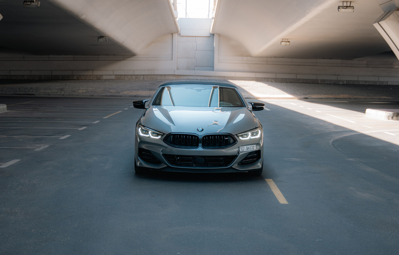Gray BMW parked in minimalist concrete parking structure with sunlight