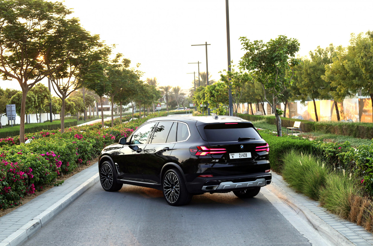 Black BMW X5 SUV parked on tree-lined street with colorful flowers