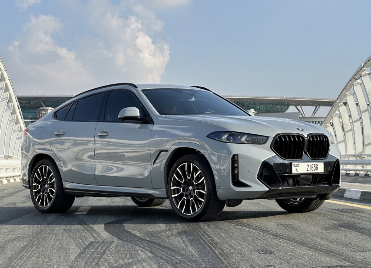 Silver BMW X6 SUV parked on a bridge with modern architecture background