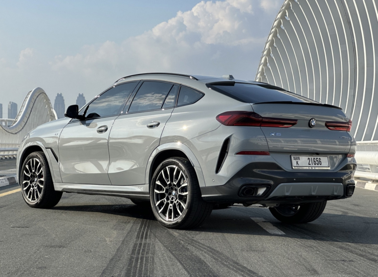 Silver BMW X6 SUV parked on road with modern curved bridge background