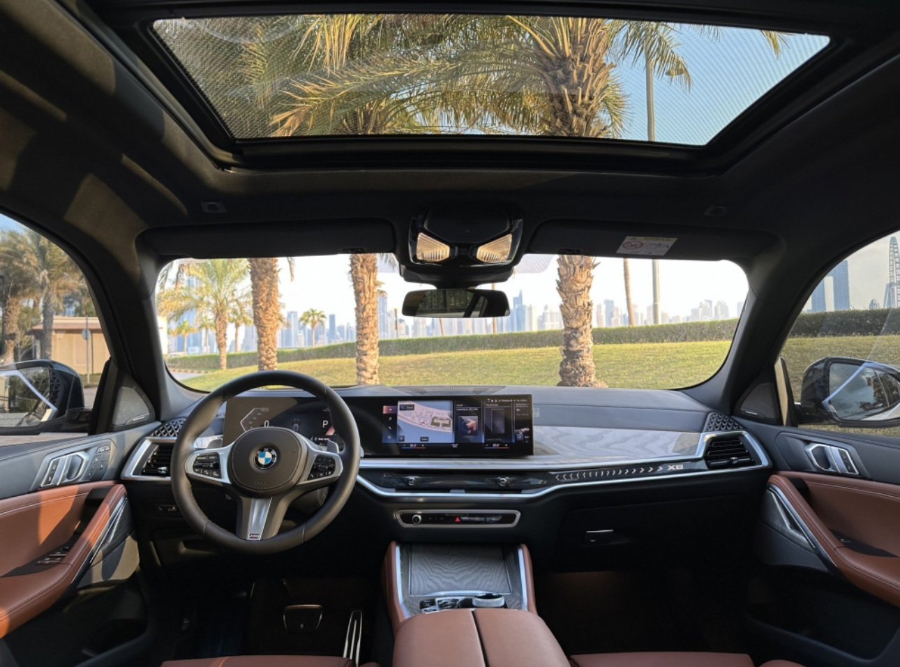 BMW interior with panoramic sunroof, palm trees, and city skyline view