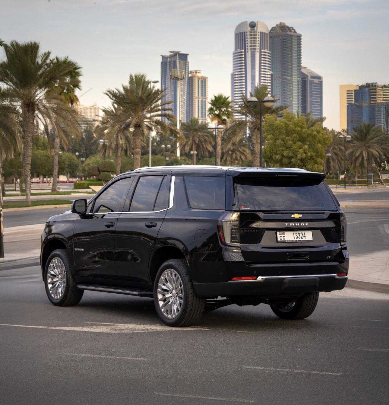 Black Chevrolet Tahoe parked near palm trees with city skyscrapers background