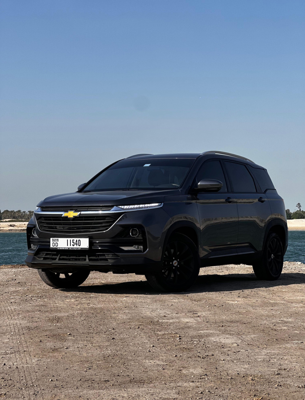 Black Chevrolet SUV parked on rocky ground near water on clear day