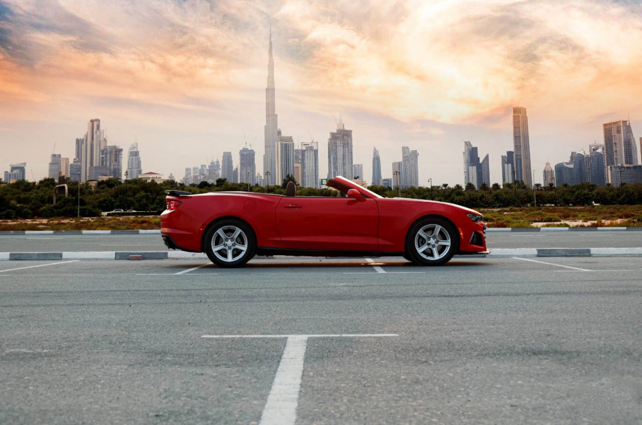 Red convertible sports car parked with Dubai skyline at sunset