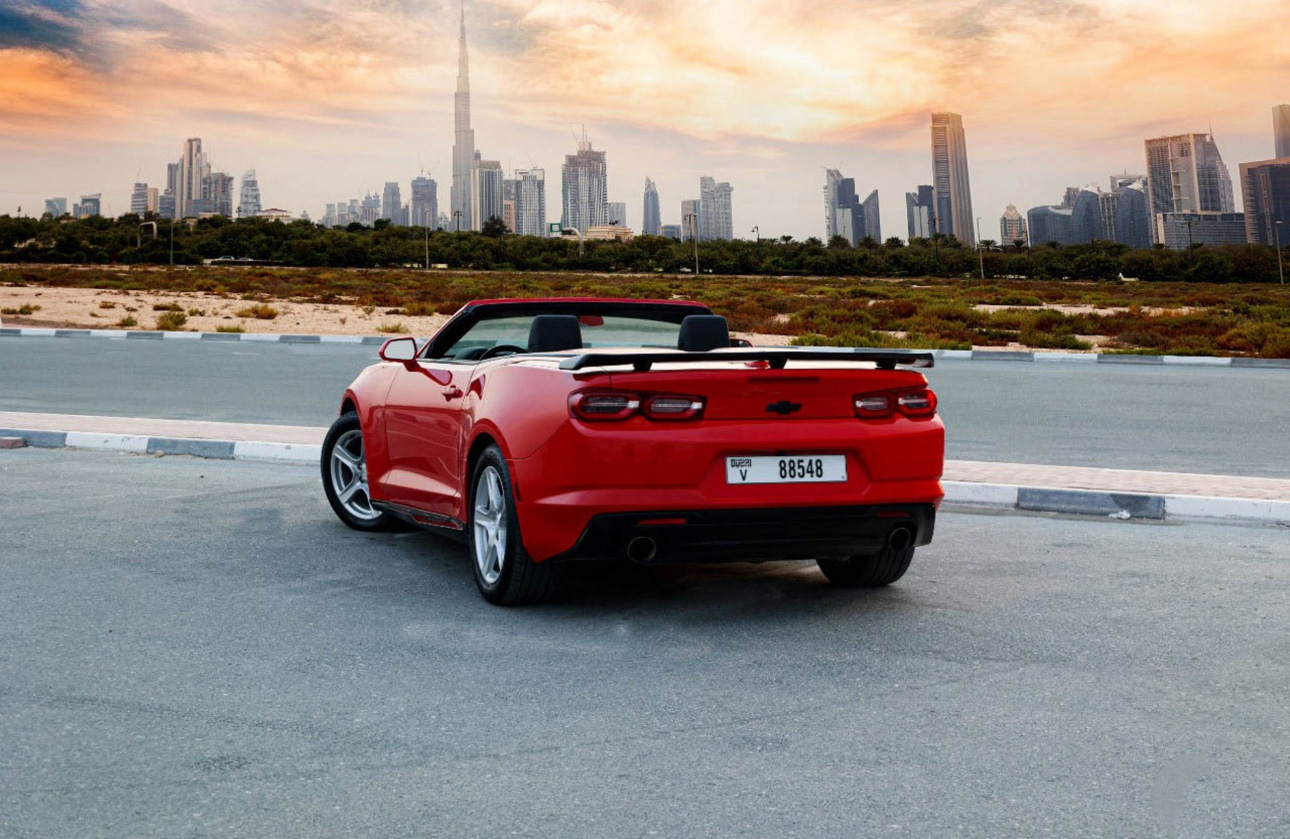 Red convertible Camaro parked with Dubai skyline at sunset