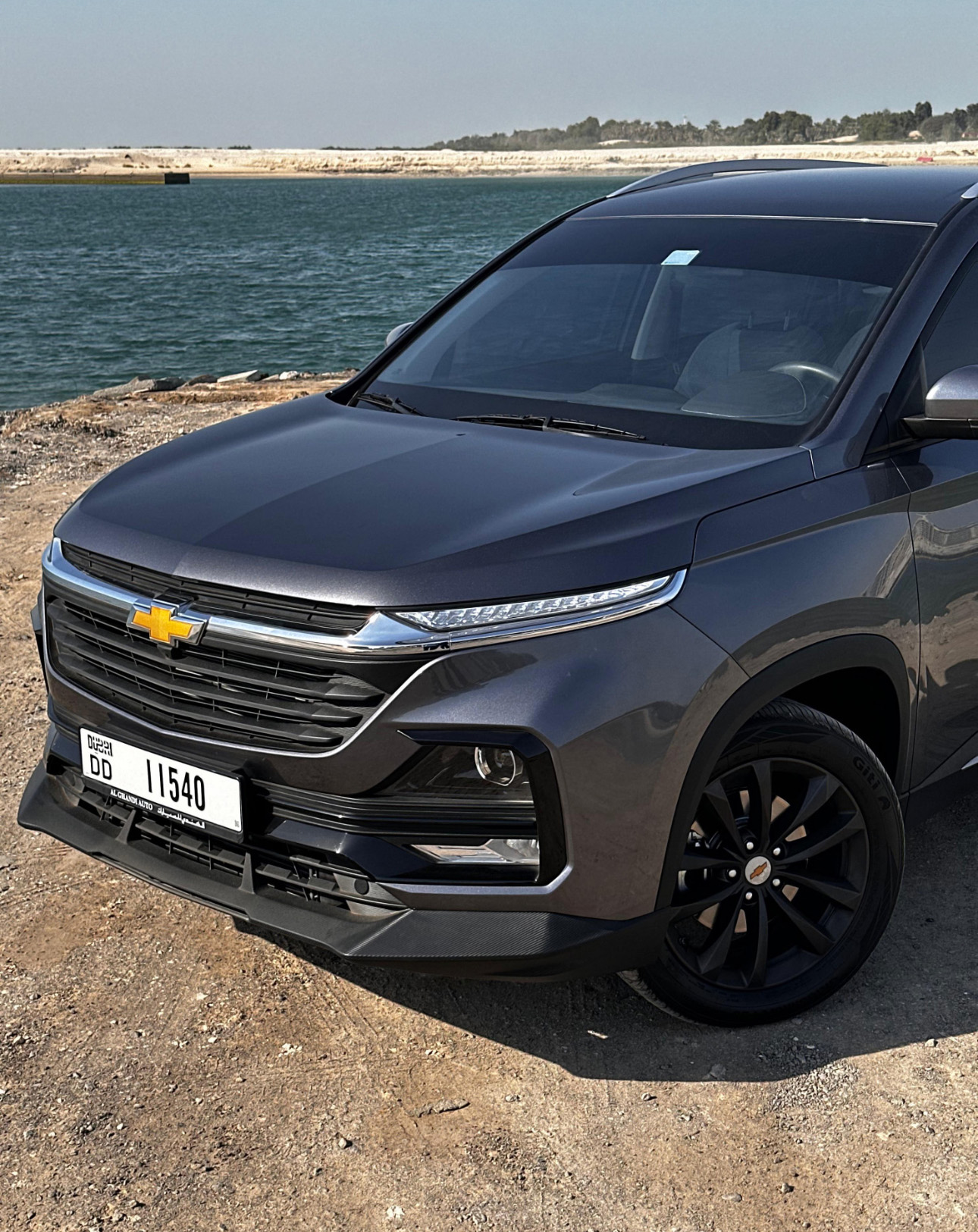 Black Chevrolet SUV parked by the ocean on rocky terrain