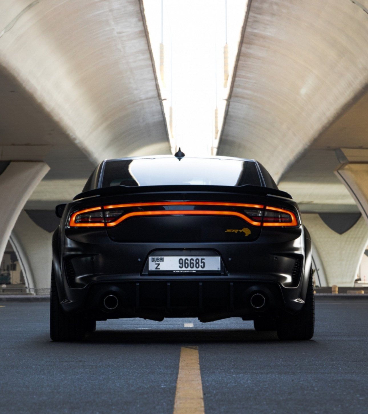 Black sports car with glowing orange taillight in modern concrete tunnel