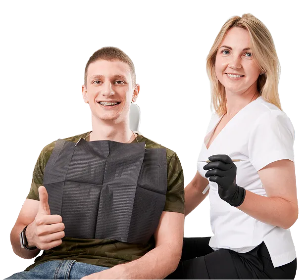 Happy dental patient giving thumbs up after treatment, seated next to a smiling female dentist in gloves, promoting professional oral care and confident smiles at a modern dental clinic.