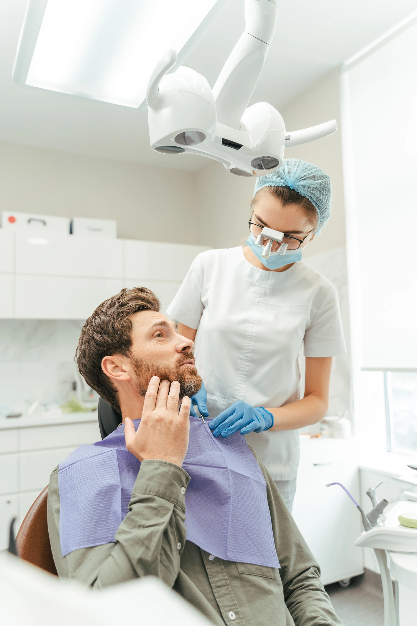 Male dental patient touching his jaw while speaking with a masked female dentist during a consultation in a modern clinic.