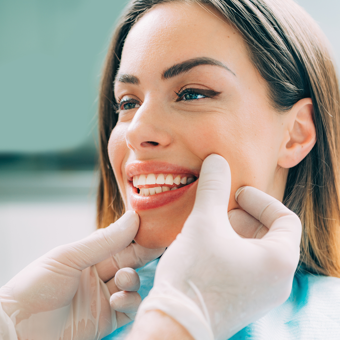 Smiling female dental patient being examined by a gloved dentist during a cosmetic or oral health evaluation.