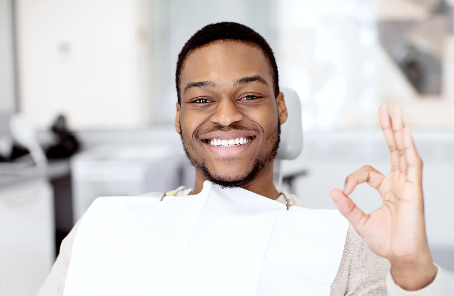 Smiling male dental patient giving an OK hand gesture while sitting in a dental chair after treatment.
