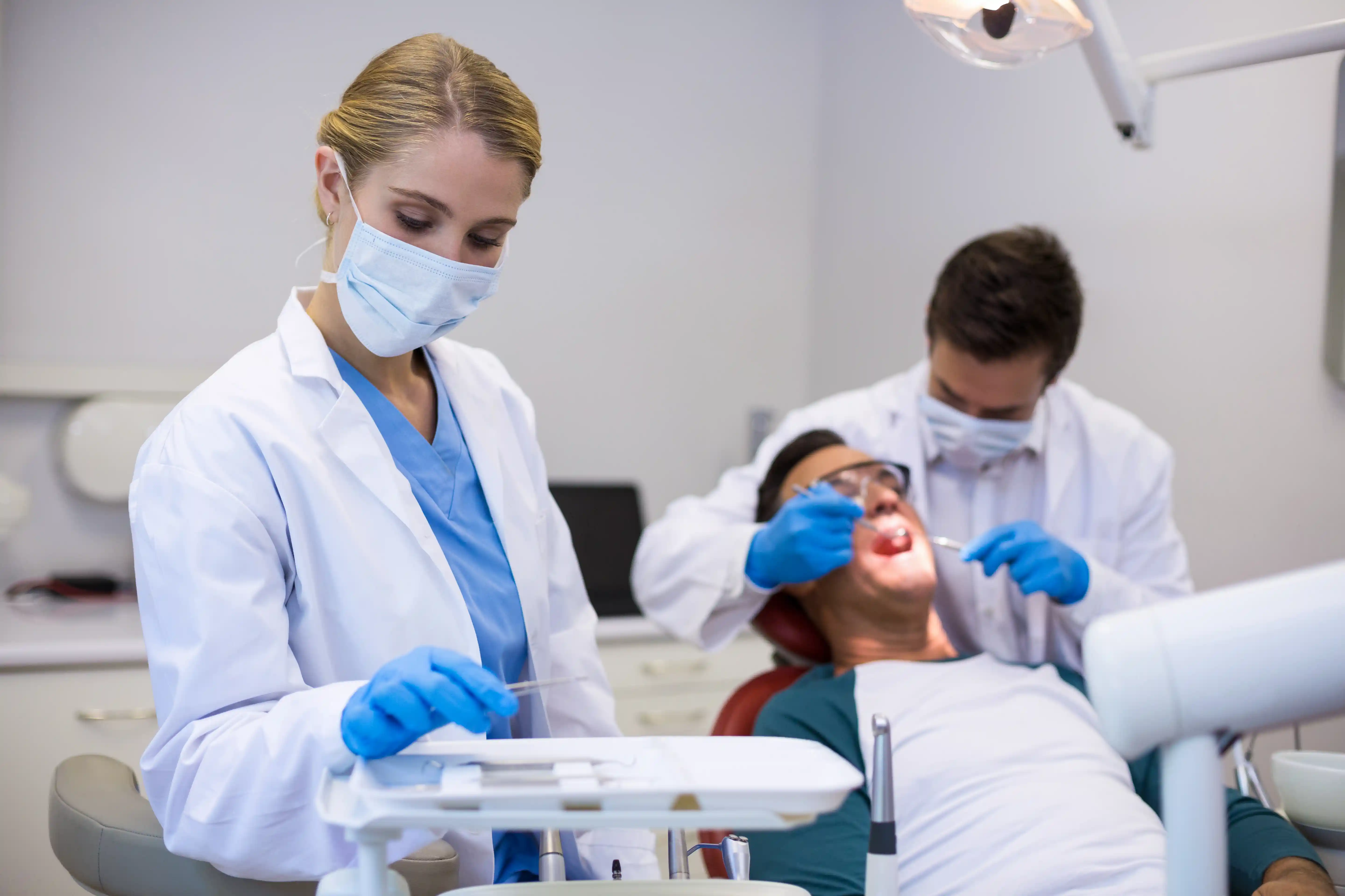 Dentist and assistant in full protective gear, including gloves, masks, and gowns, providing dental treatment to a patient in a clean and sterile environment