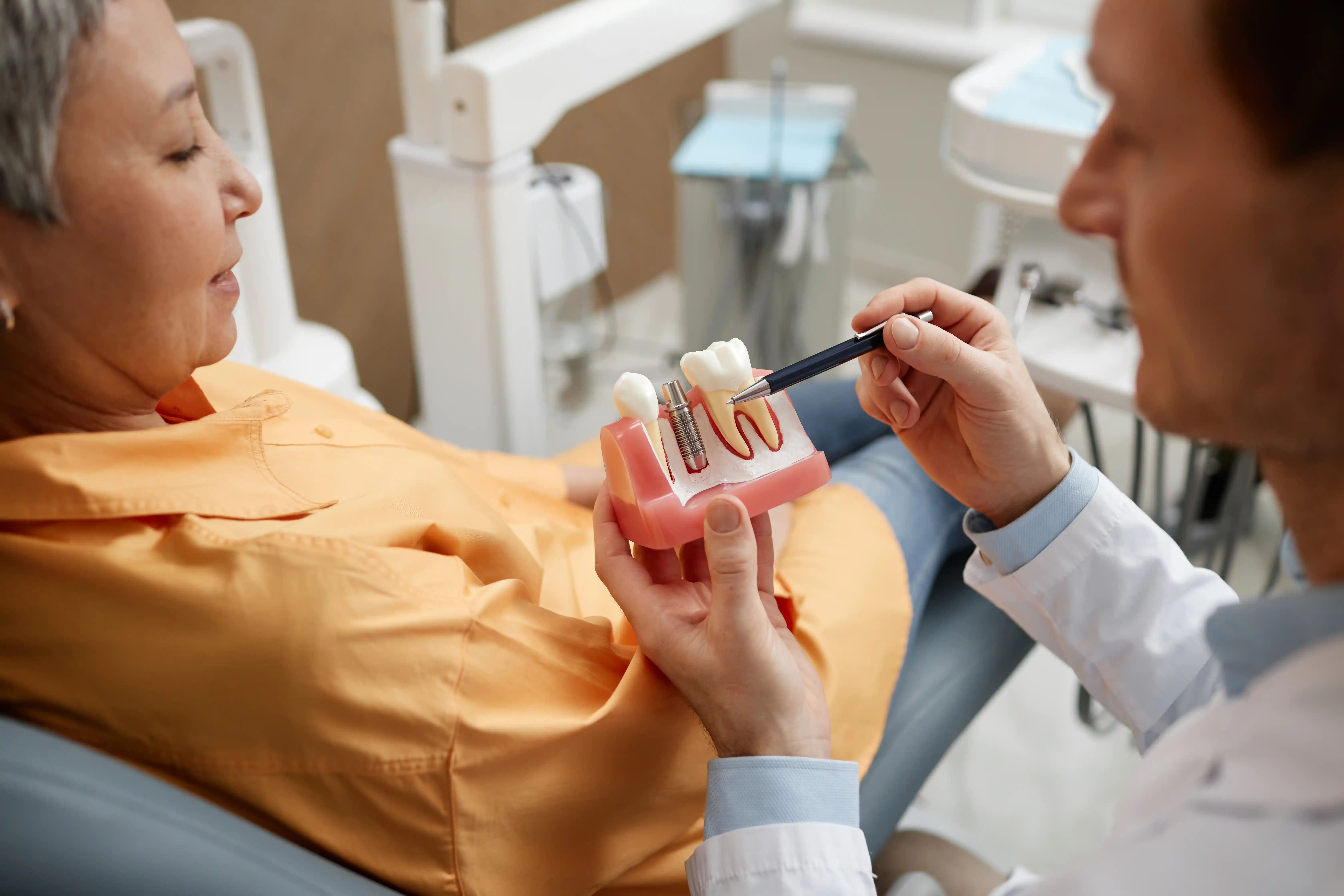 Close-up of a dentist performing a dental procedure on a reclining patient, using specialized dental instruments while the patient wears a protective bib