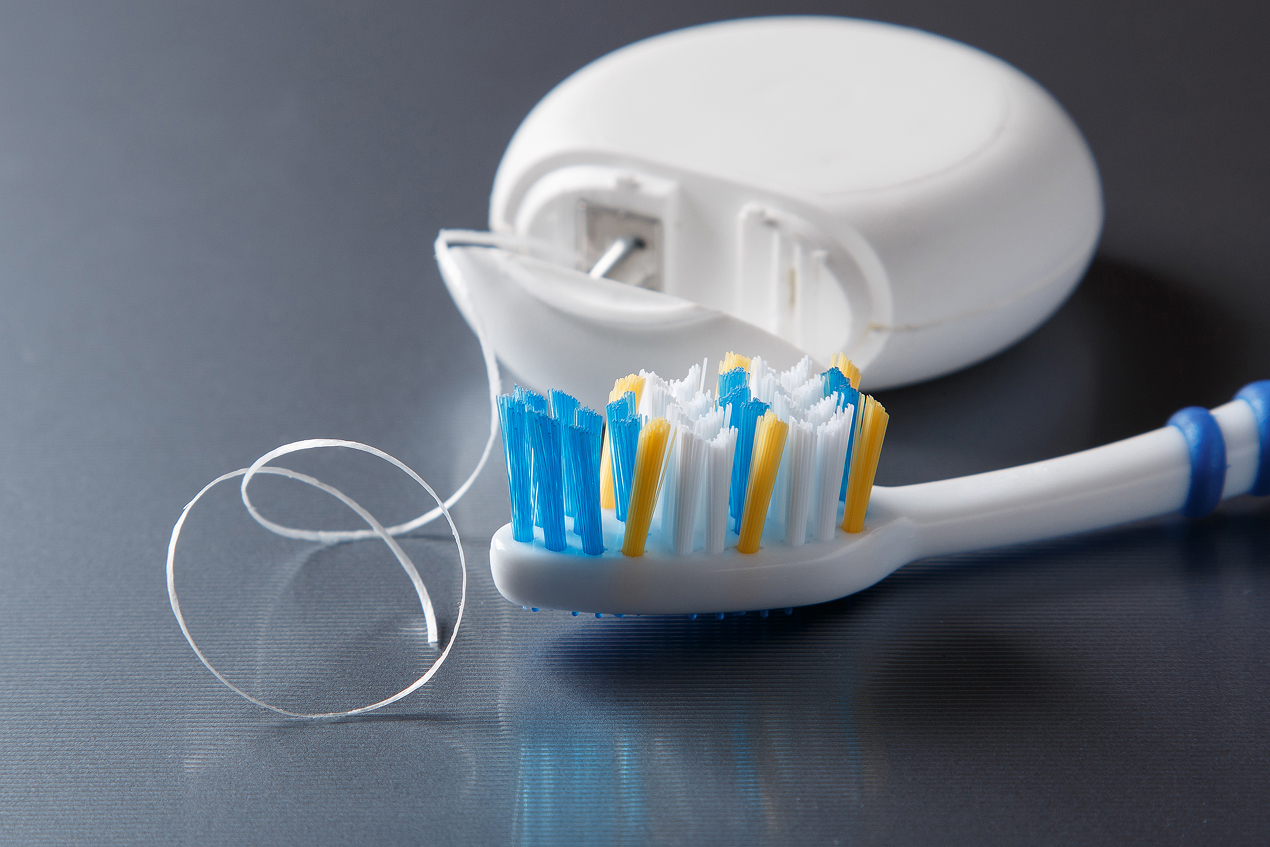 Close-up of a toothbrush and dental floss container on a bathroom counter for daily dental care.