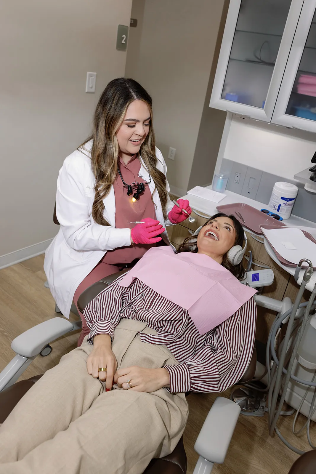 Two Method Modern Dentistry team members in rose scrubs leaning together and smiling at the front desk in Alpharetta, GA