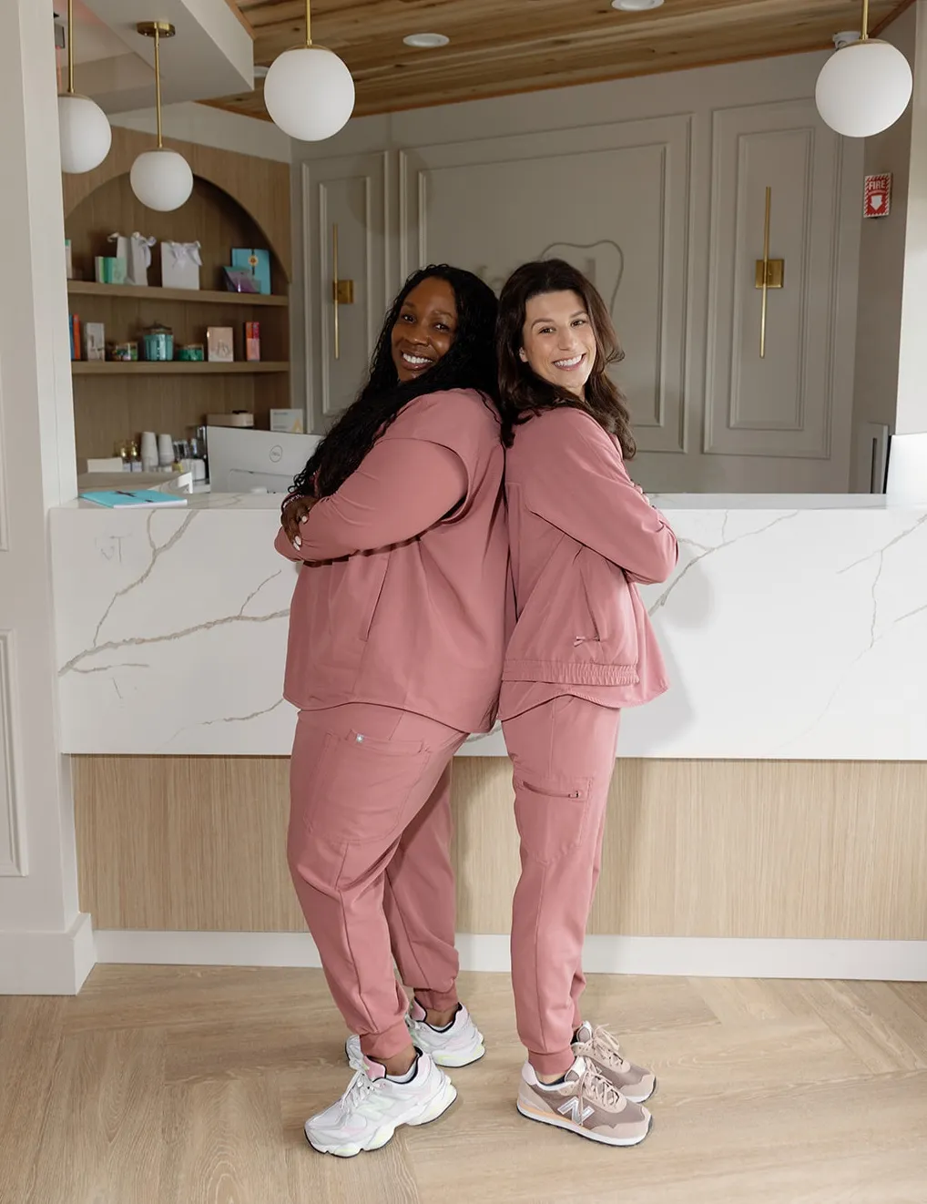 Two Method Modern Dentistry team members in rose scrubs leaning together and smiling at the front desk in Alpharetta, GA