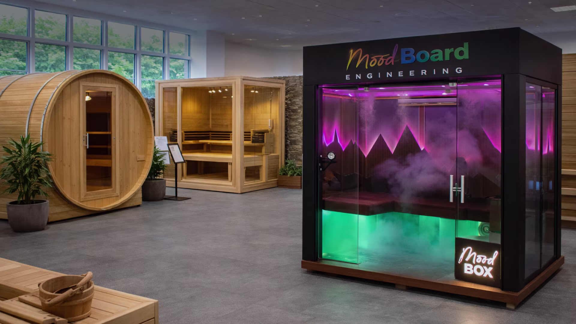 Modern wellness area with two wooden saunas and a black glass-enclosed Mood Box emitting colorful purple and green lights with fog inside.
