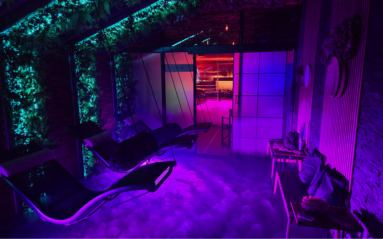 Indoor lounge area with hanging chairs, purple and blue ambient lighting, and a fog-covered floor.