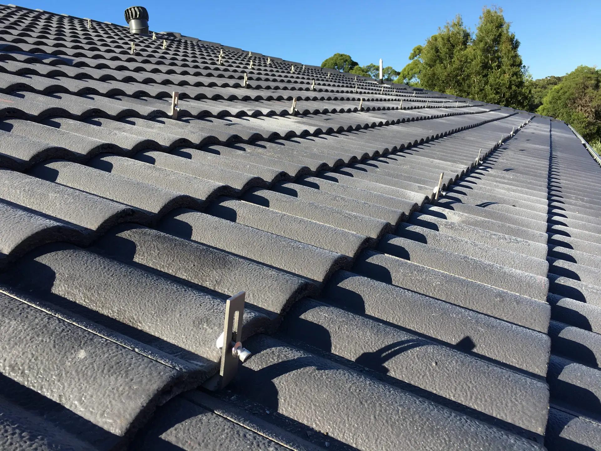 Clenergy mounting brackets installed on a concrete tile roof with precisely ground tiles sitting flush around each bracket — Solarbank installation, Sydney
