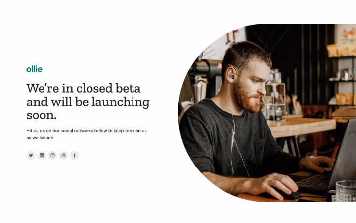 Man with earphones working on laptop at a wooden table in a cozy cafe setting.