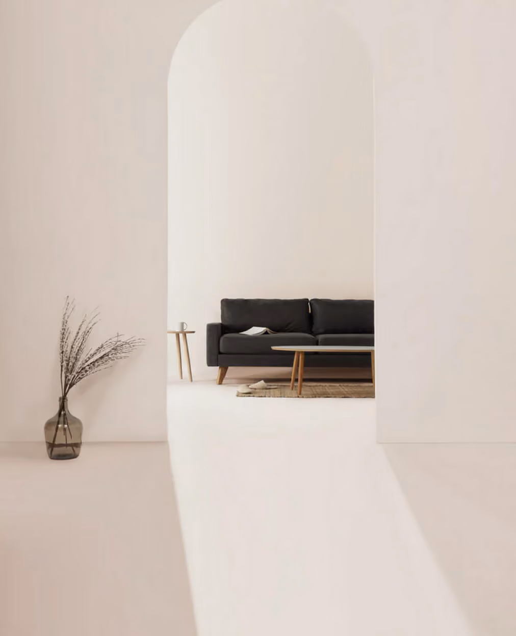 Minimalist living room with black sofa, wooden coffee table, side table, and tall vase with dried branches.