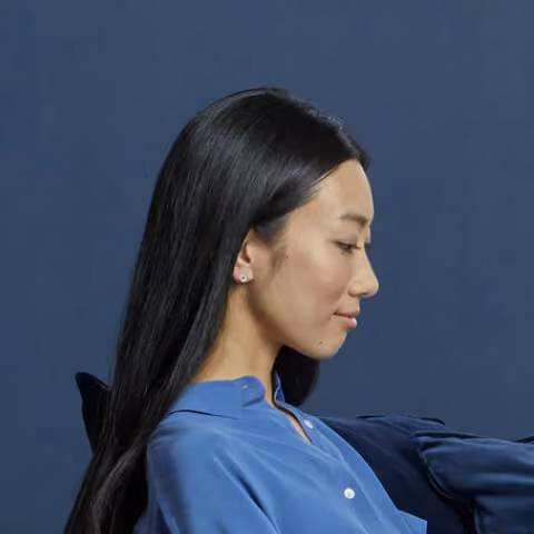 Profile of a woman with long black hair wearing a blue blouse against a dark blue background.