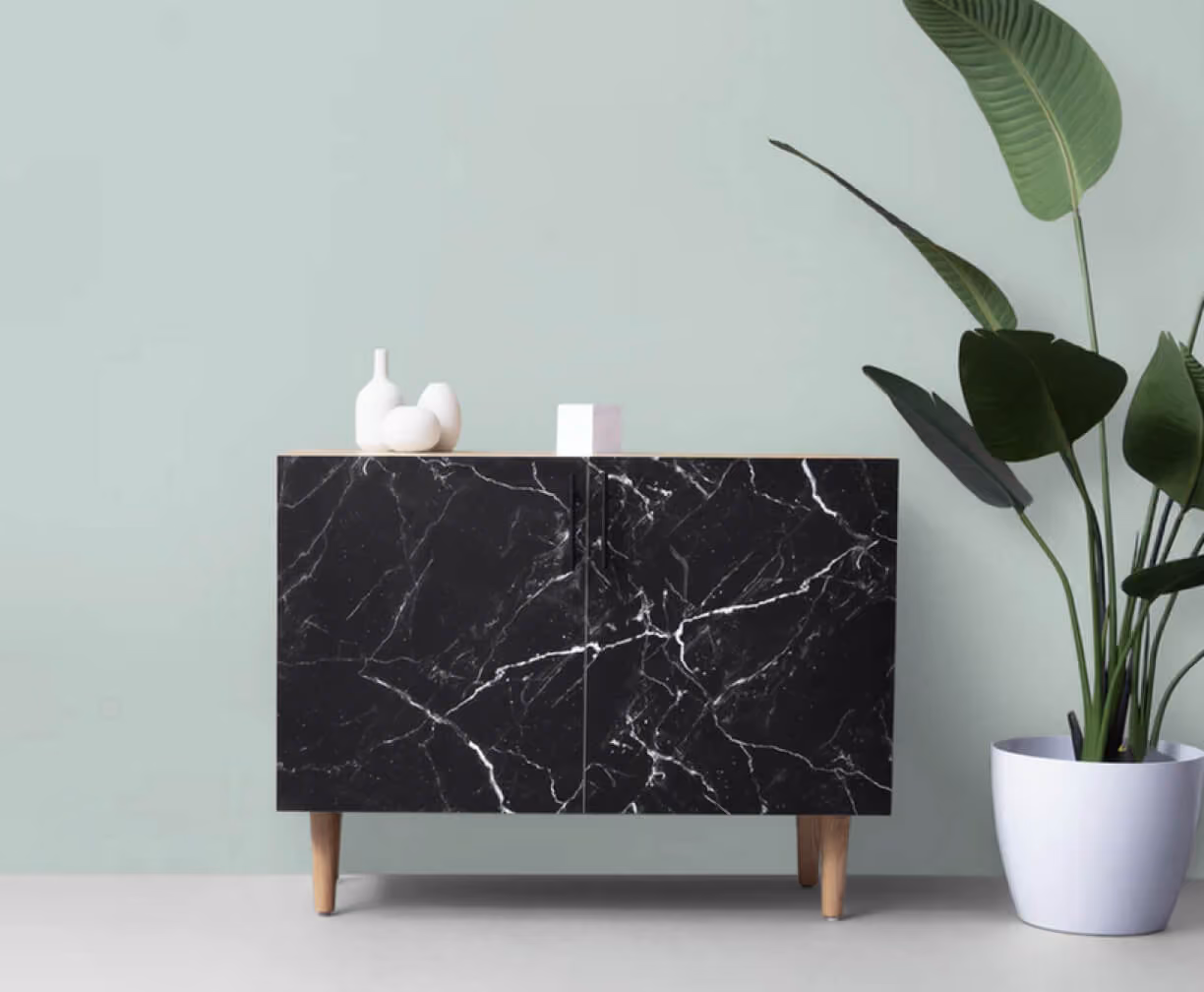 Black marble cabinet with wooden legs and white decor, next to a potted tropical plant.