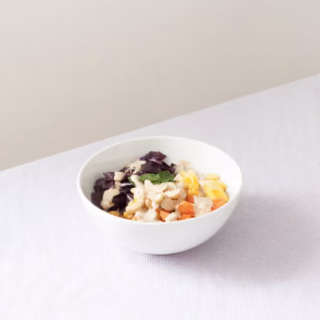 White bowl with cashews, chopped purple cabbage, corn, carrots, and a mint leaf on a white surface.