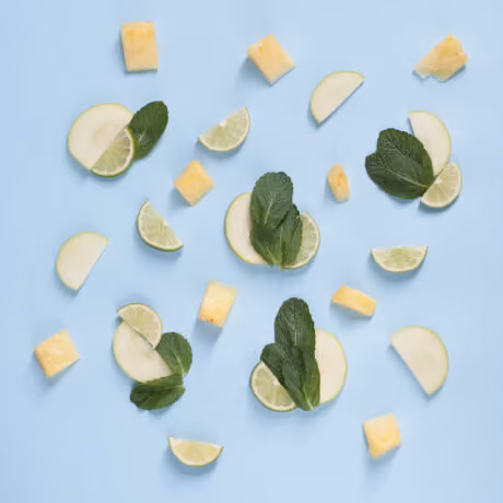 Slices of lime, apple, pineapple chunks, and mint leaves scattered on a light blue background.
