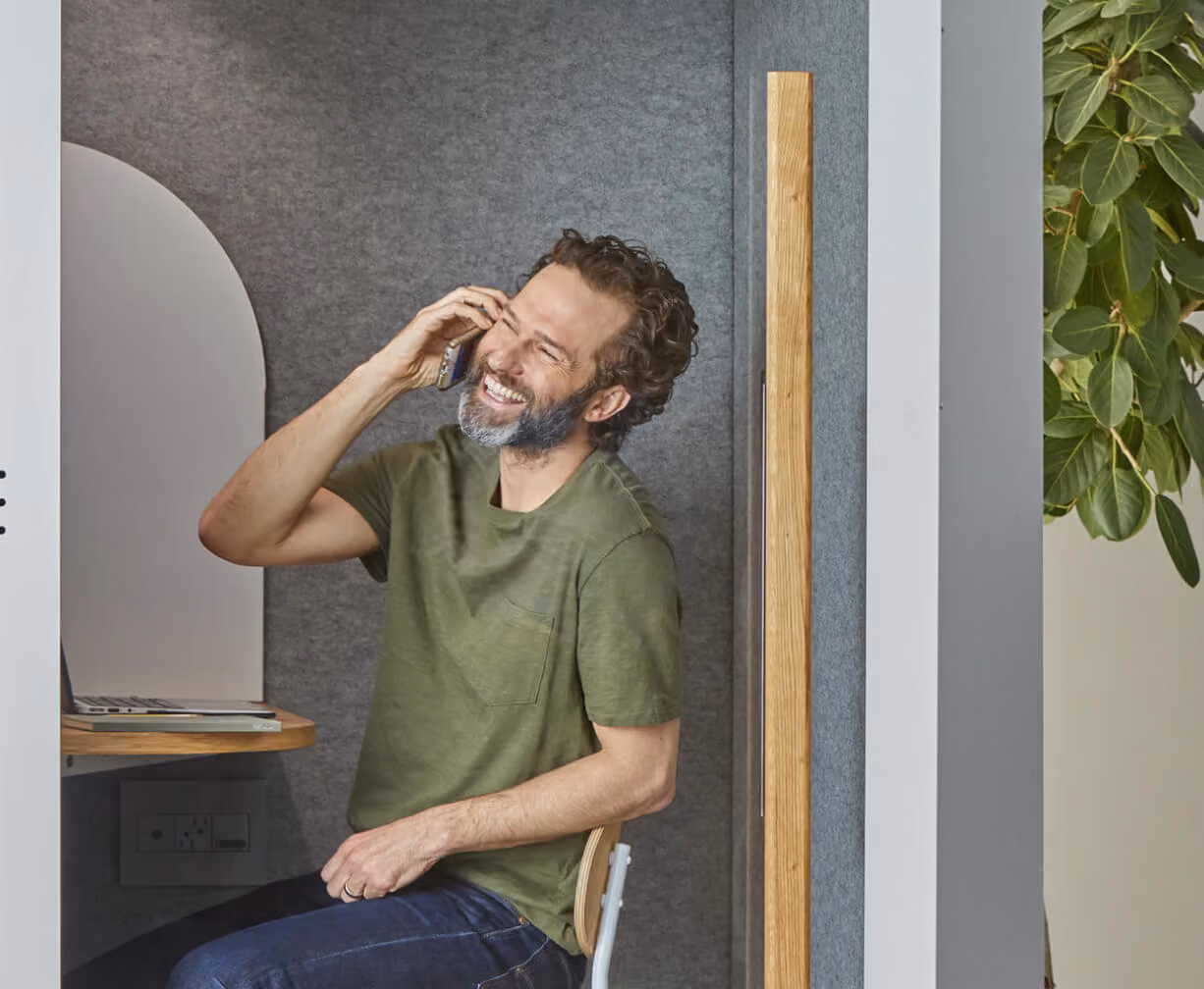 Smiling man in green shirt sitting in a small booth and talking on the phone.