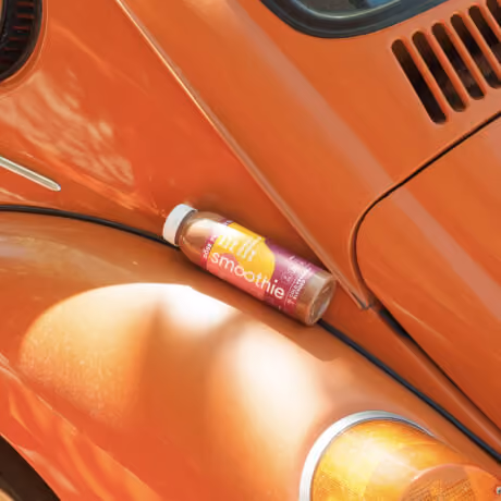 Bottle of Lift smoothie resting on the fender of an orange vintage car in sunlight.