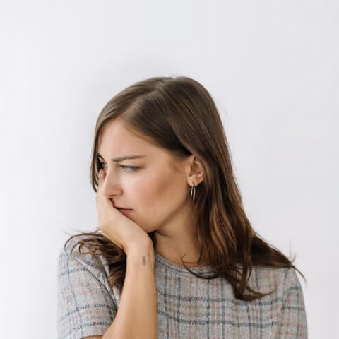 Thoughtful young woman with brown hair, resting her chin on her hand, looking to the side.