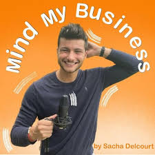 Un homme souriant tenant un microphone devant un fond orange avec le texte courbé « Mind My Business » au-dessus.