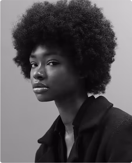 Black and white portrait of a young woman with a large afro hairstyle wearing a dark jacket, looking directly at the camera.