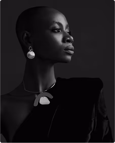 Black and white portrait of a woman with a shaved head wearing large round earrings and a statement necklace, looking to the side.
