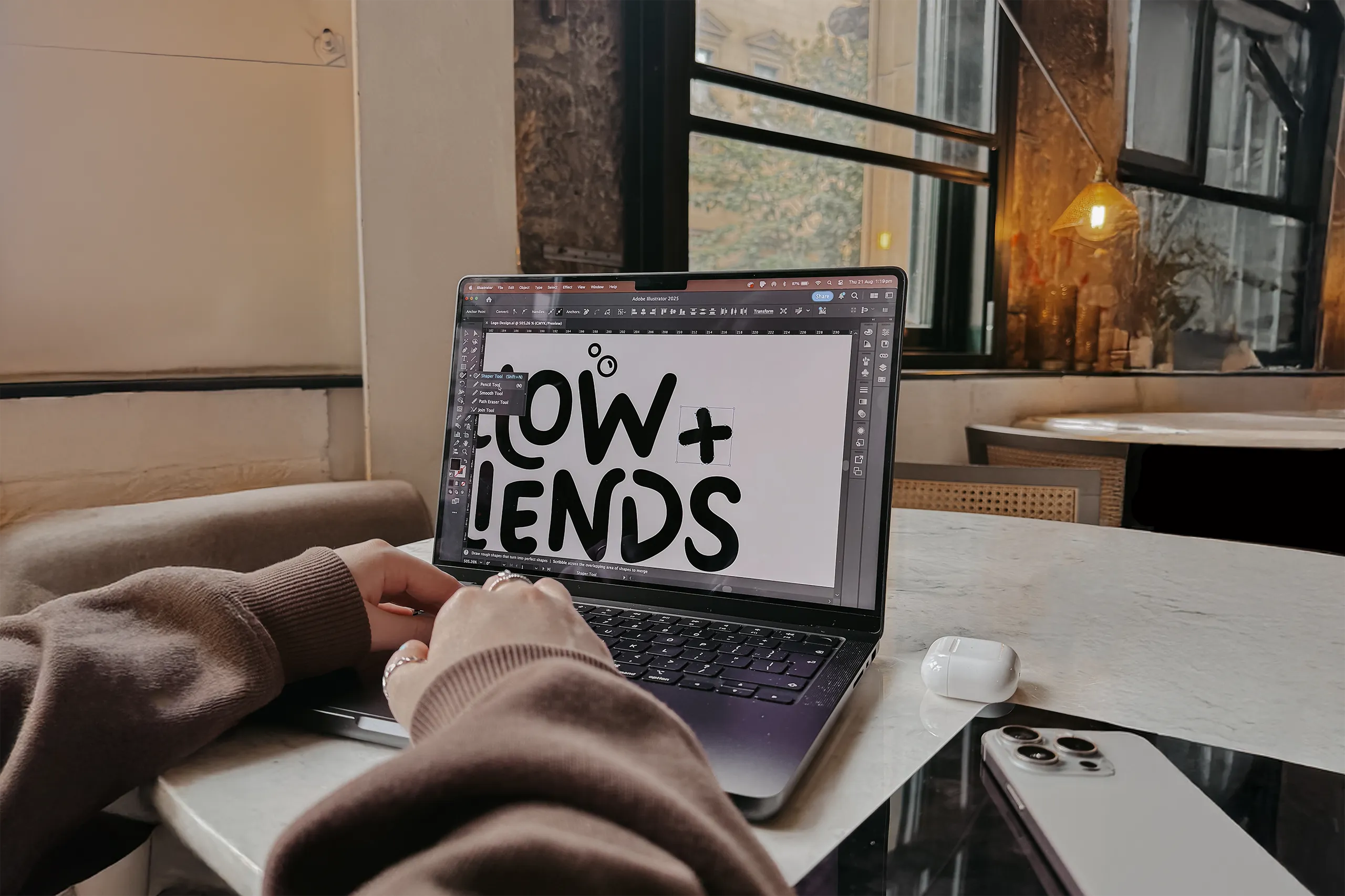 Person using a laptop with Adobe Illustrator open, editing bold black text reading 'LOW + ENDS' on the screen.