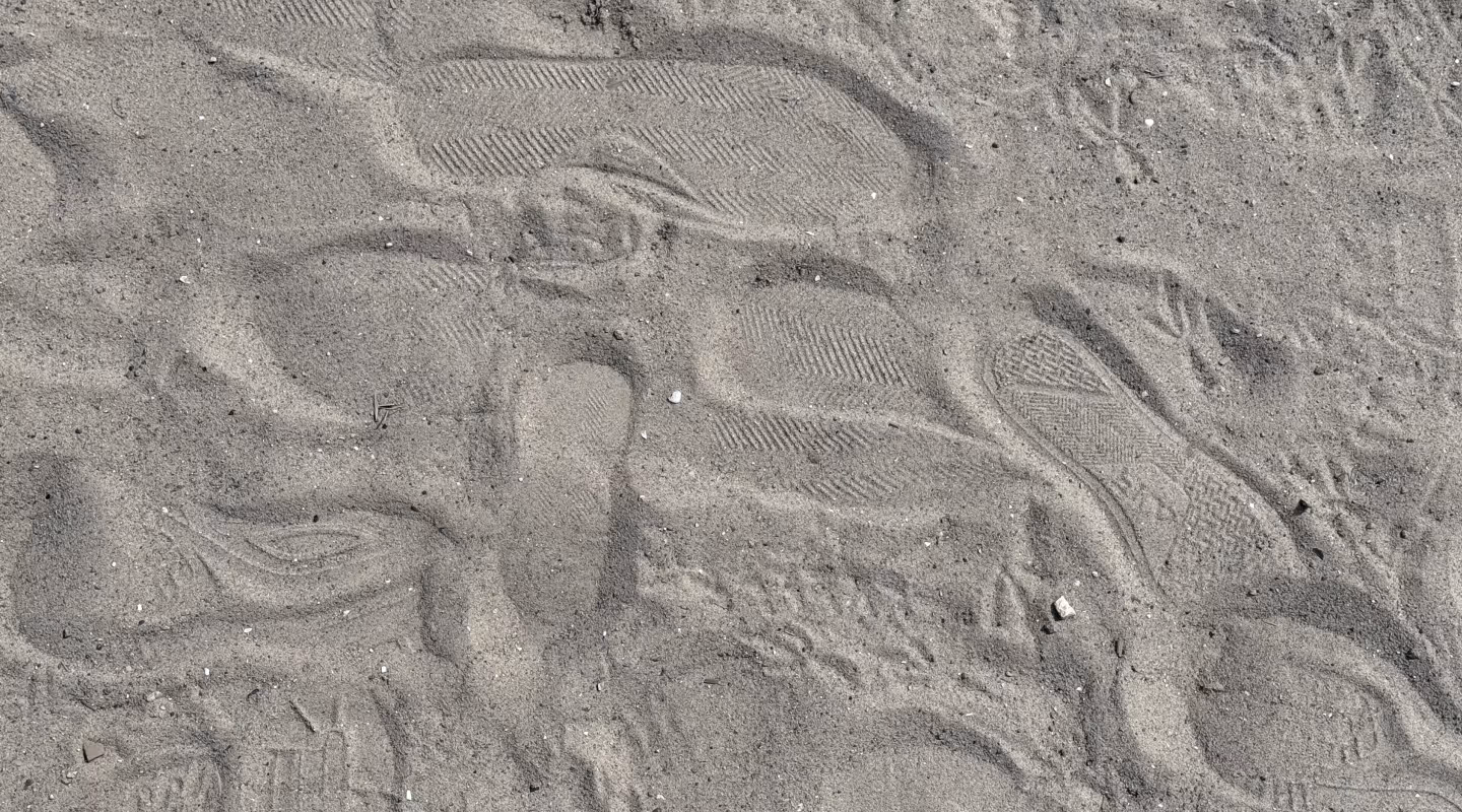 Multiple overlapping shoe prints with various tread patterns imprinted in dry sand.