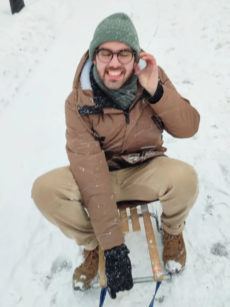 Savvas is laughing sitting on a small sleigh witha a snowy background