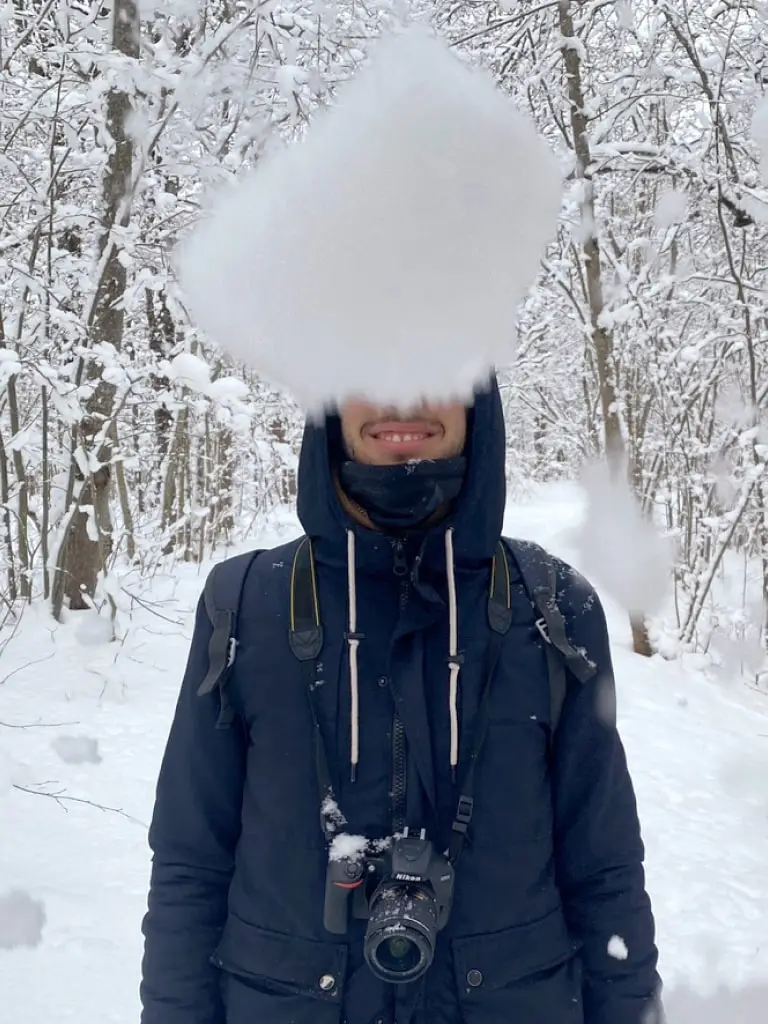 Antonis is about to get hit by a huge snowball covering his head in a snowy forest.