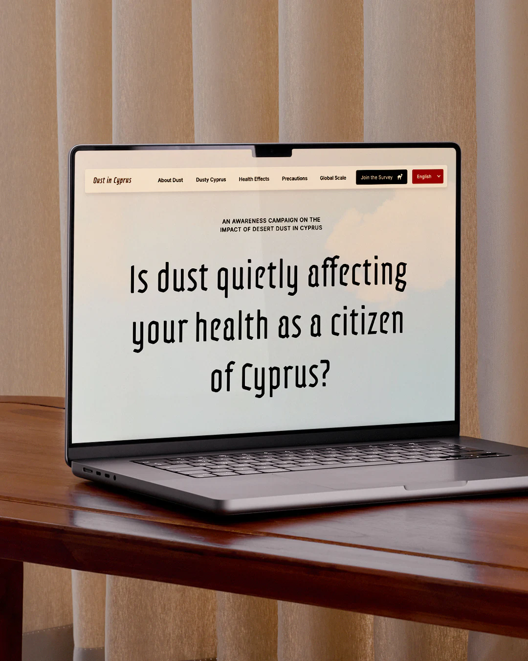 Laptop on wooden table showing Dust in Cyprus campaign website with bold health impact question